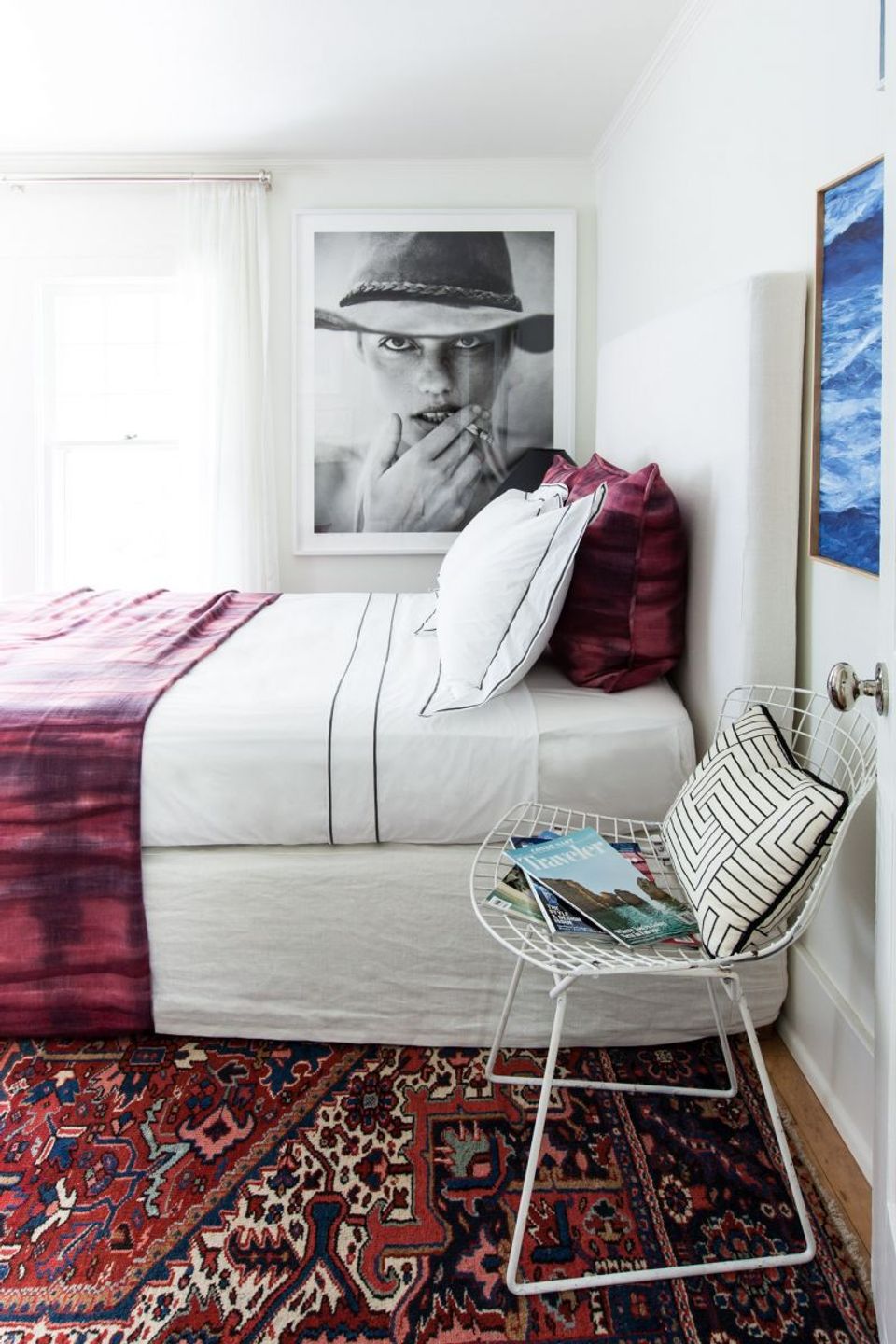 Eclectic bedroom blending burgundy accents, black-and-white portrait, and vintage patterned rug