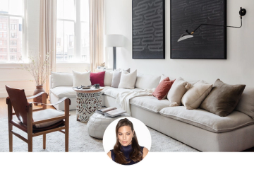 Warm minimalist living room with cream sectional, earth-tone pillows, black abstract art, and natural light from tall windows