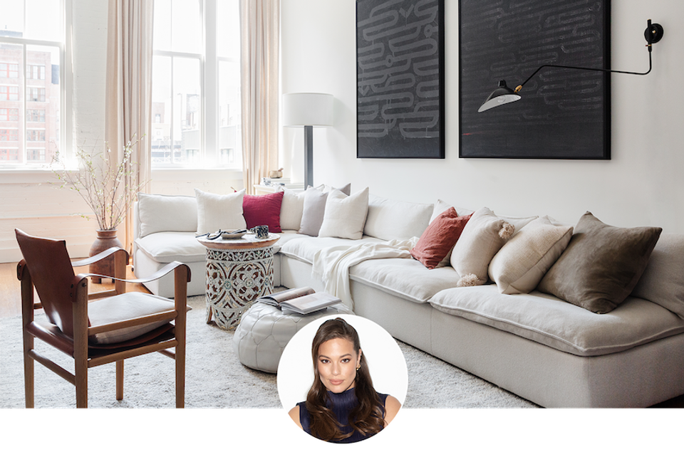 Warm minimalist living room with cream sectional, earth-tone pillows, black abstract art, and natural light from tall windows
