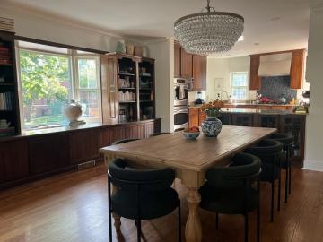 Warm transitional kitchen-dining space blending dark cabinetry, natural wood dining table, soft lighting, and cozy built-in window seating.