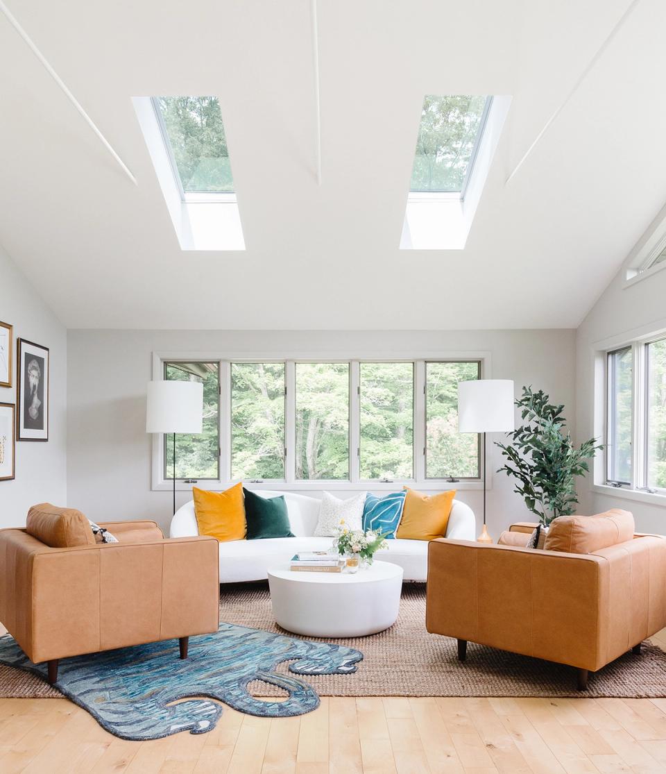 Modern airy living room with caramel leather chairs, white seating, blue geometric rug