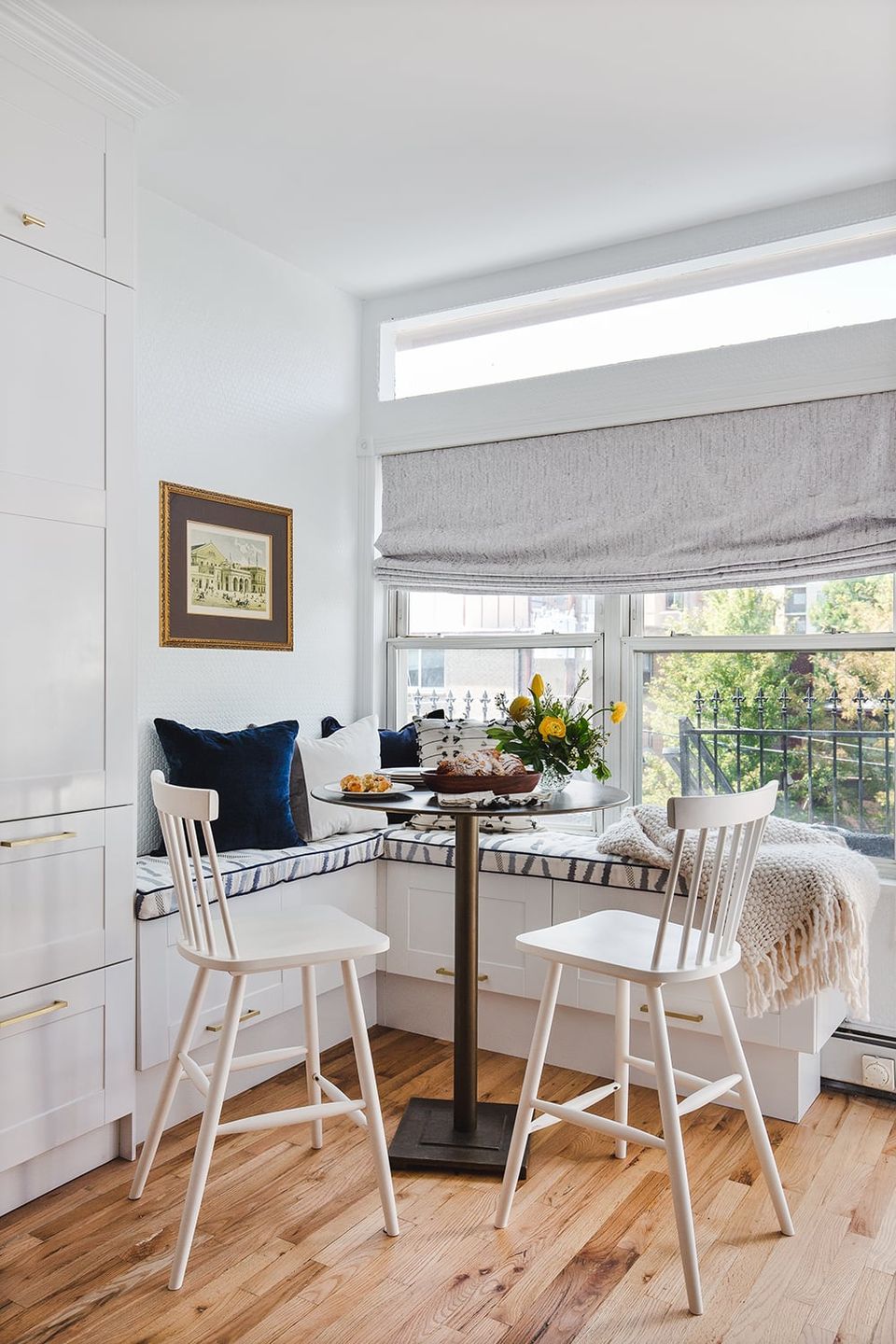 Modern breakfast nook with window seating, white chairs, natural light, and layered textiles creating a cozy intimate dining atmosphere