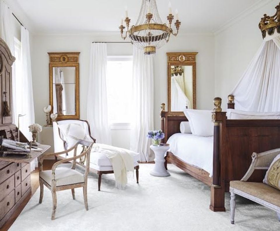 Luxe New Orleans bedroom with dark wood bed, gold mirrors, sheer white curtains, and classical chandelier