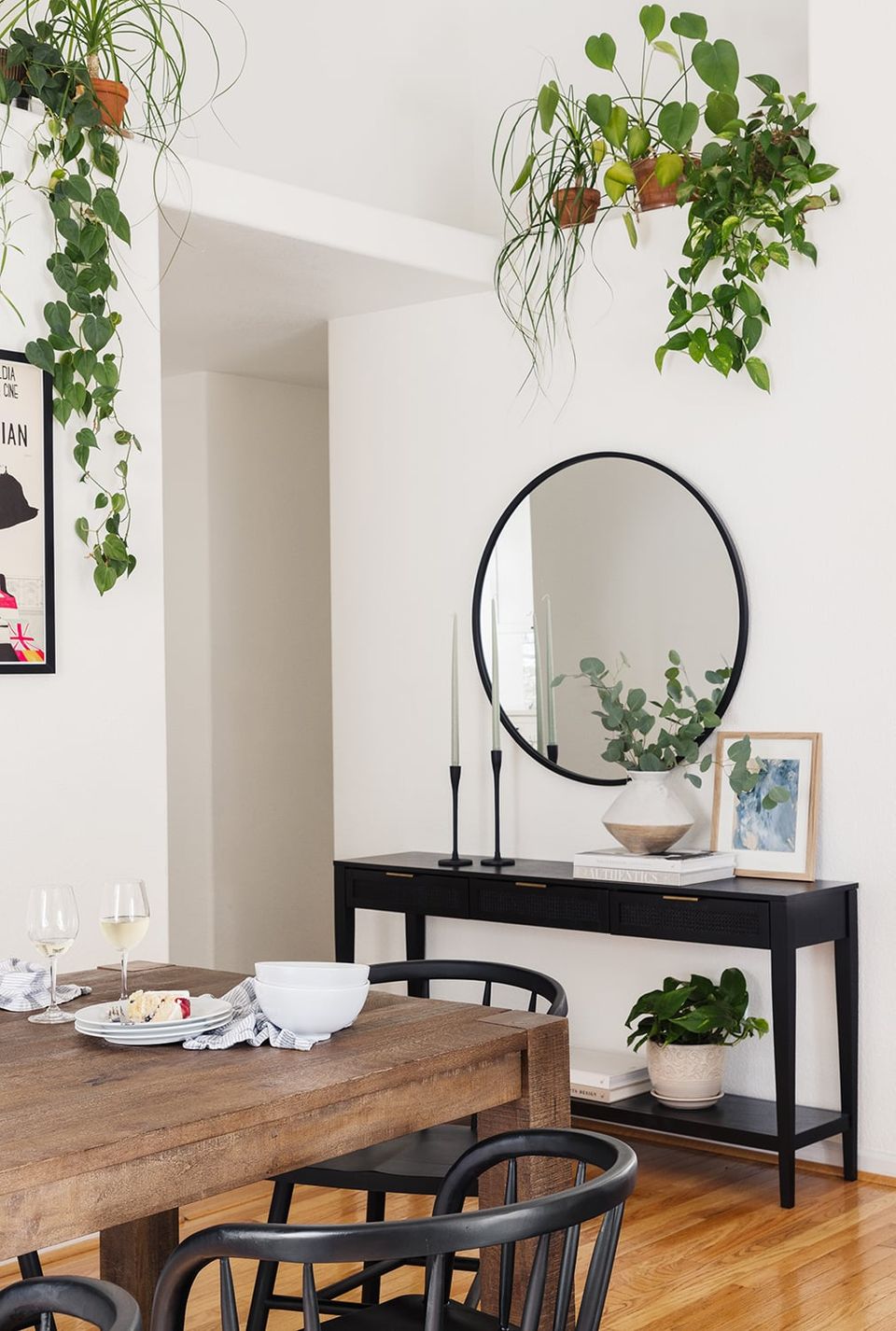 Minimalist modern dining area with black console, round mirror, hanging plants, and natural wood tones emphasizing clean elegance