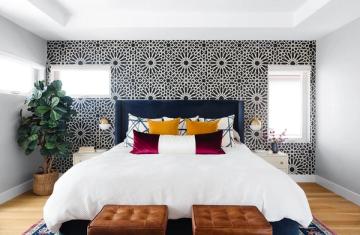 Modern bedroom with geometric patterned accent wall, navy headboard, colorful pillow mix, and warm wood flooring