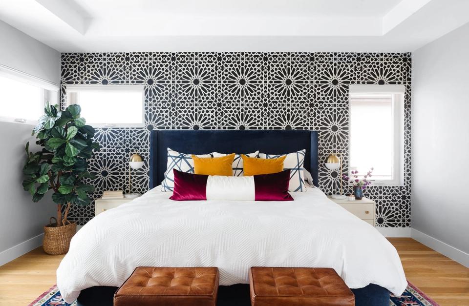 Modern bedroom with geometric patterned accent wall, navy headboard, colorful pillow mix, and warm wood flooring