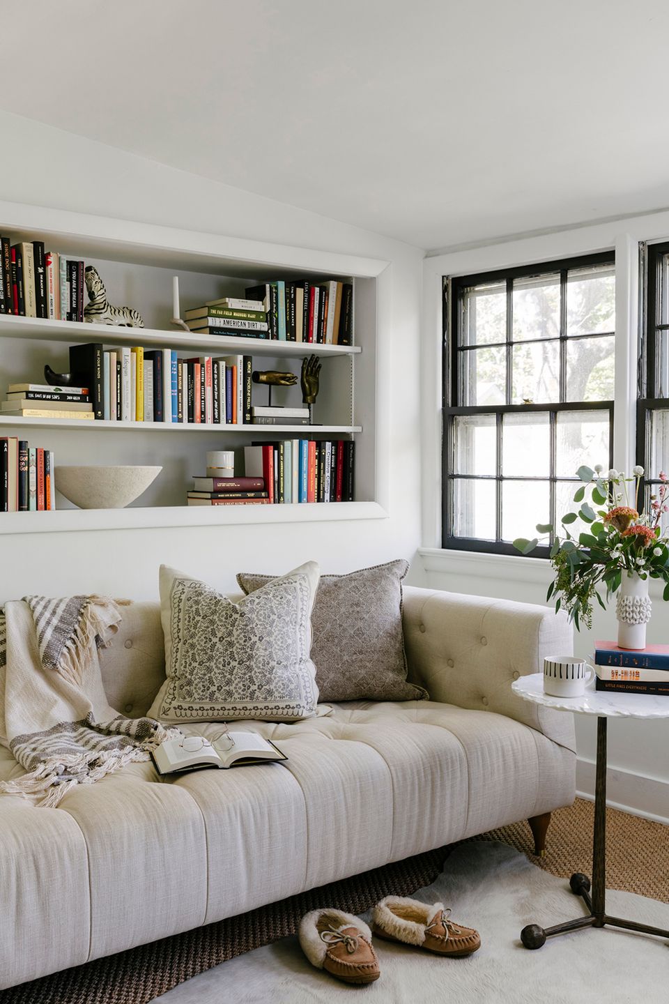 Minimalist reading nook with window seat, built-in shelving, soft neutral upholstery, and natural light creating calm atmosphere