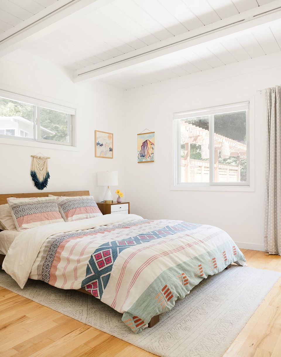 Bright cottage bedroom with patchwork quilted bedding, wooden bed frame, and cheerful multi-colored wall art