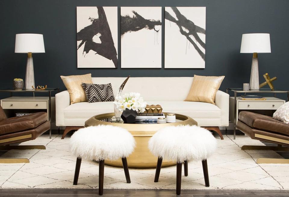 Modern living room with slate blue walls, cream sofa, and gallery art above. Mid-century wood nightstands flank the space with warm, layered lighting and geometric accents.
