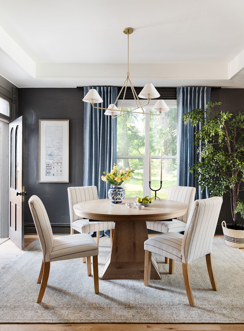 Contemporary dining space with dark charcoal walls, cream striped chairs, round wood table, and lush green plant accents