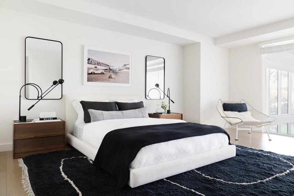 Mid-century modern bedroom with warm wood bed, black and white bedding, dark area rug, and sculptural mirrors.