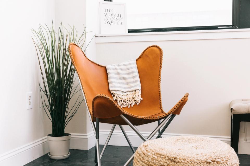 Mid-century modern office corner with cognac leather butterfly chair, potted grass plant, and woven poufs in warm neutrals