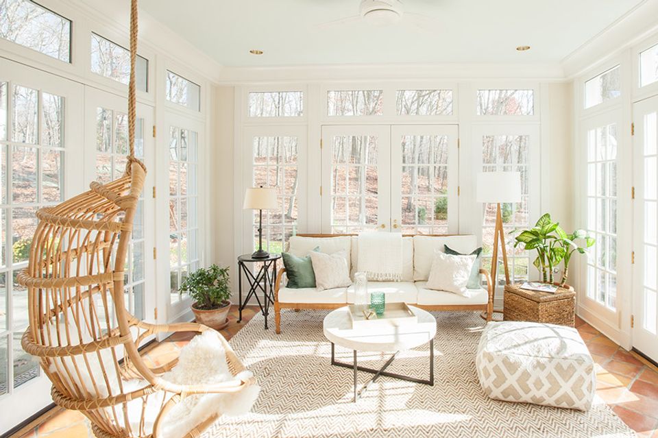 Tranquil sunroom with woven rattan hanging chair, cream furnishings, abundant natural light, botanical accents