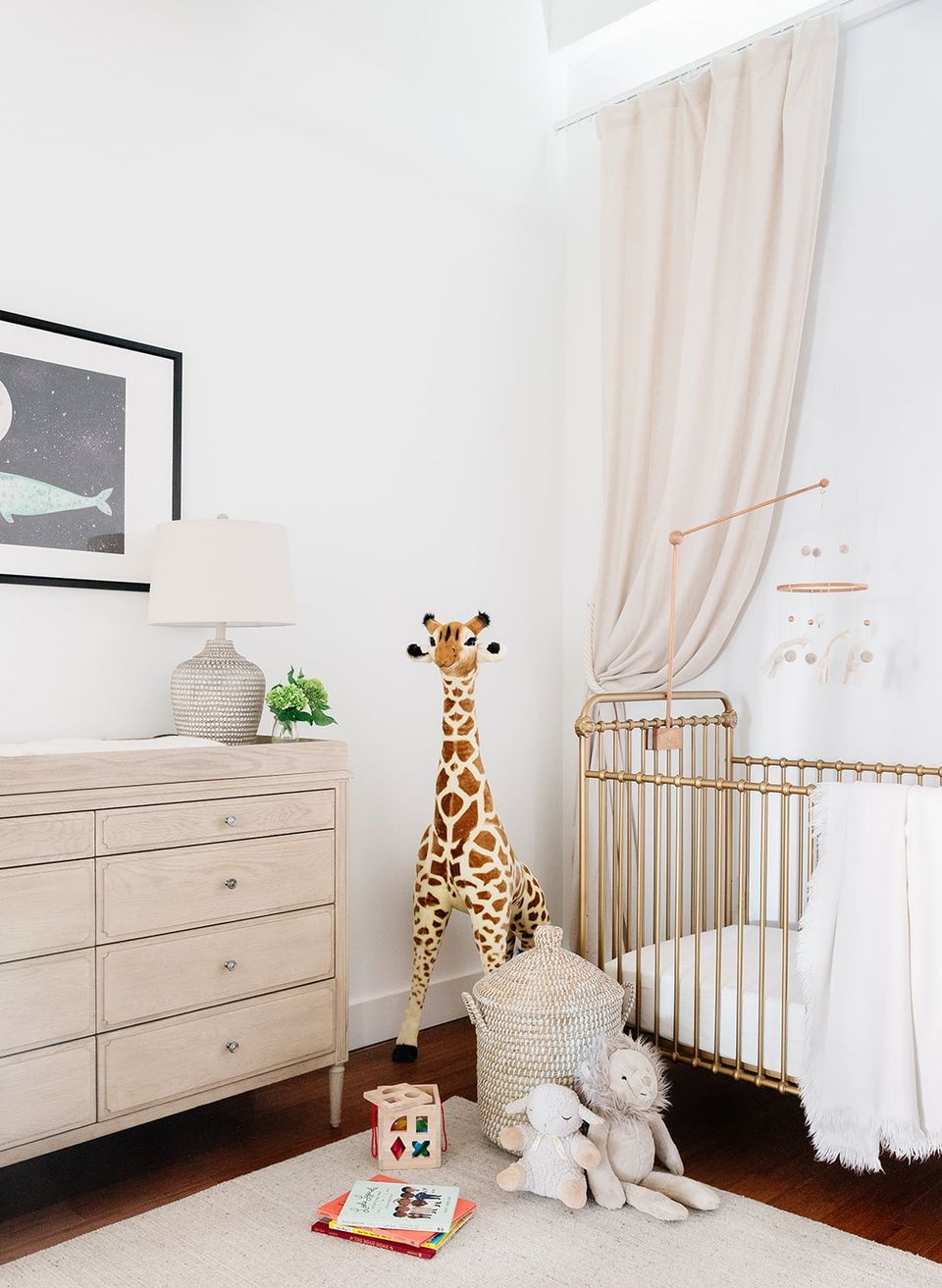 Minimalist safari nursery in warm beige with giraffe sculpture, wooden dresser, and soft elegance