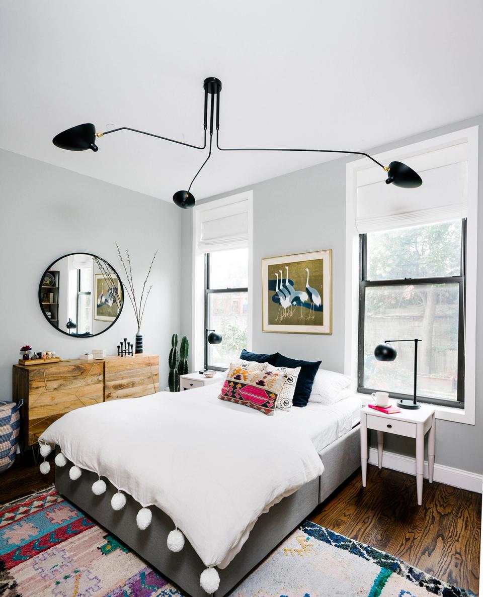 Modern mid-century bedroom with sculptural black ceiling fixture, wood dresser, white bedding, colorful rugs, and art.
