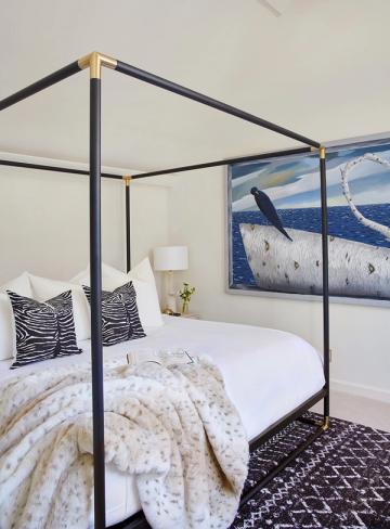 Sophisticated coastal canopy bed with black metal frame, zebra-print pillows, and ocean landscape wall art