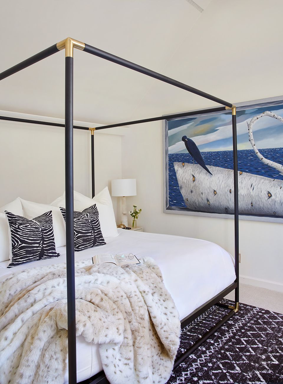 Sophisticated coastal canopy bed with black metal frame, zebra-print pillows, and ocean landscape wall art