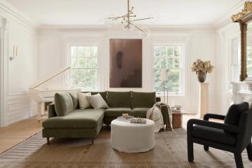 Contemporary space with olive green sectional, cream ottoman, black chair, and large windows offering a calm, refined aesthetic