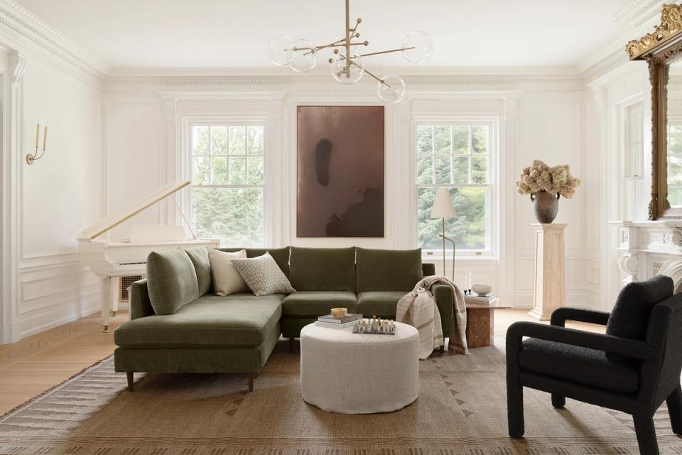 Contemporary space with olive green sectional, cream ottoman, black chair, and large windows offering a calm, refined aesthetic