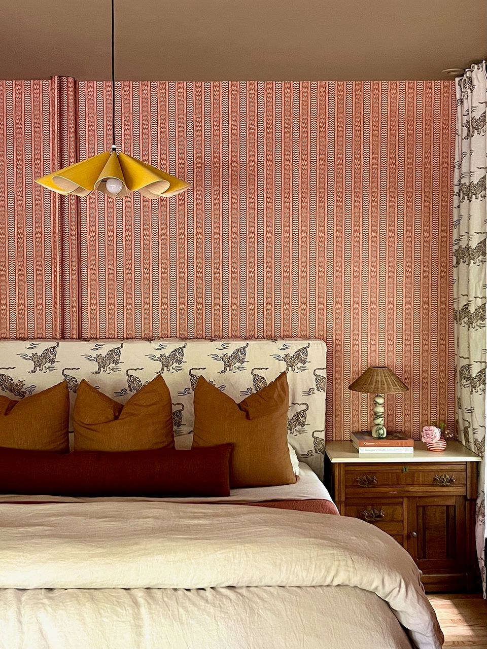 Eclectic maximalist bedroom mixing coral wallpaper, mustard pendant, and patterned upholstered headboard