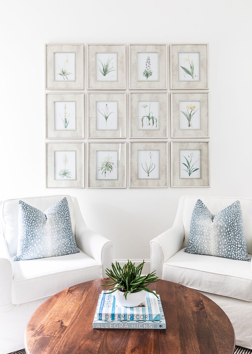 Classic living area with white chairs, blue patterned pillows, botanical gallery wall above