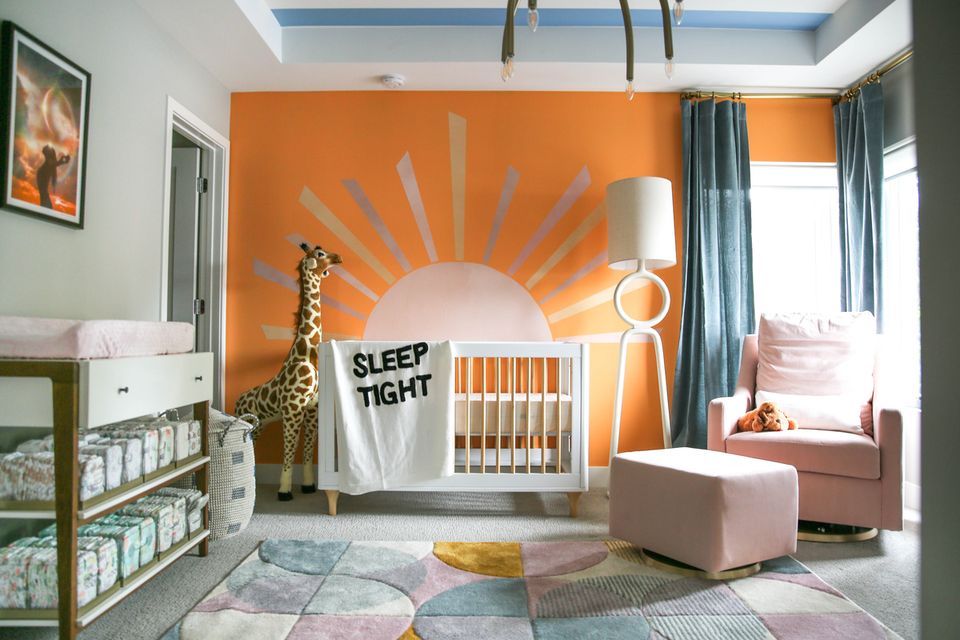 Vibrant modern nursery featuring bold orange accent wall with sun mural and playful color palette