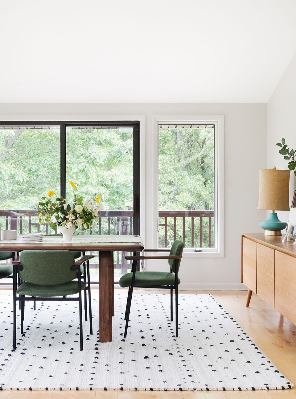 Bright mid-century dining room with green chairs, patterned geometric rug, and natural light from expansive windows overlooking greenery