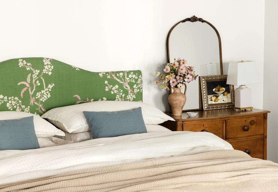 Cottage-style bedroom with green damask headboard, warm wood dresser, and soft blue pillows