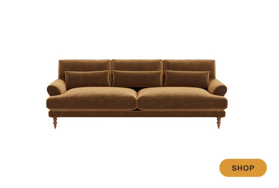 Caramel velvet sofa with curved arms and brass casters on white background