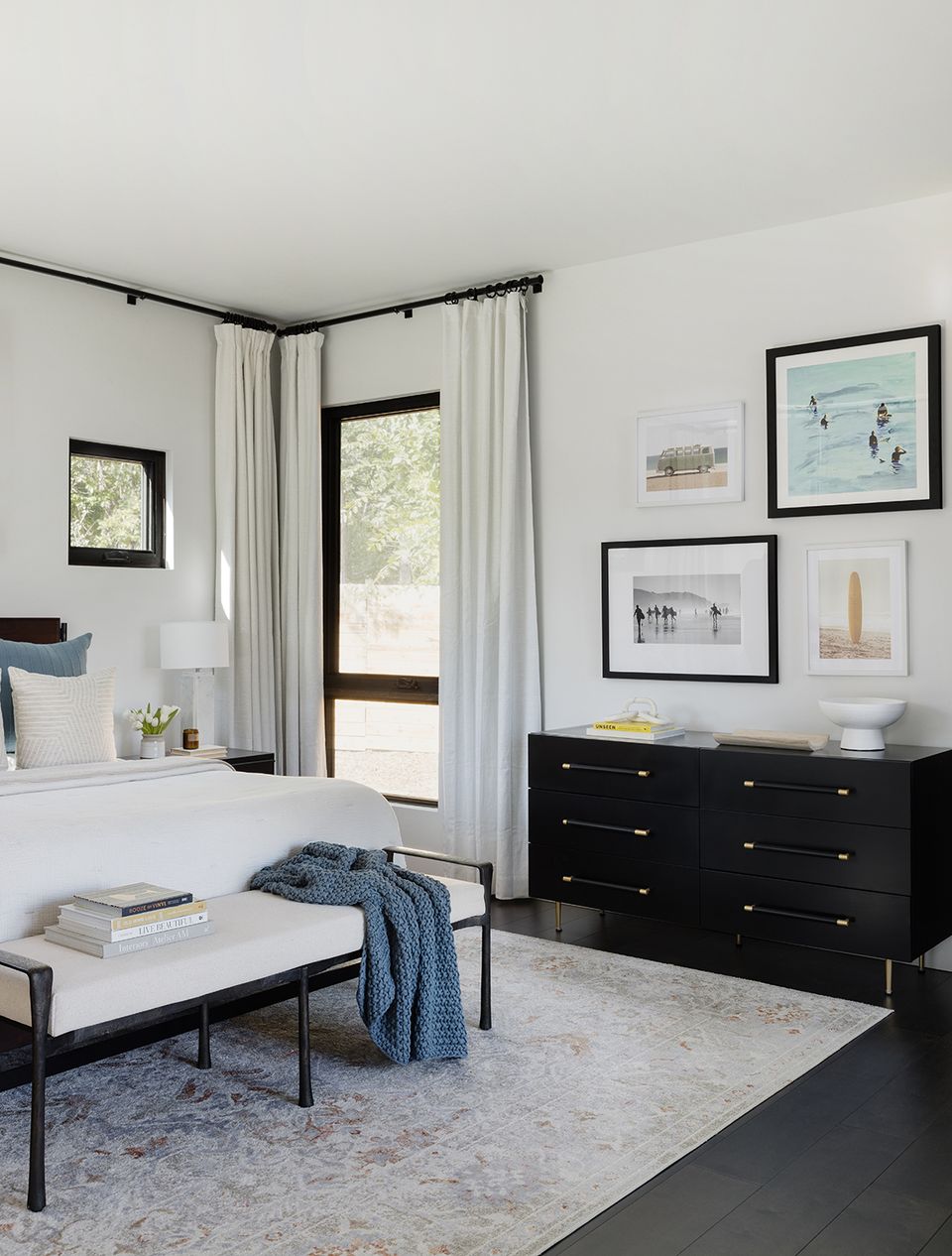 Contemporary monochromatic bedroom with black dresser, gallery wall art, flowing white curtains, and clean modern aesthetic