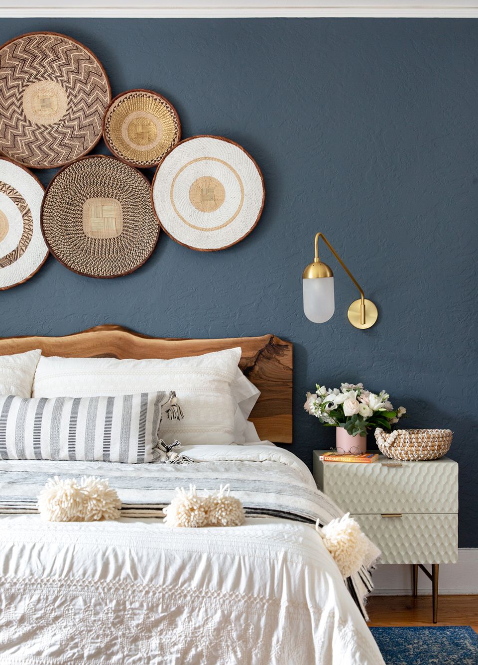Modern earthy bedroom with slate blue accent wall, woven basket wall art, warm wood headboard, and natural fiber accessories