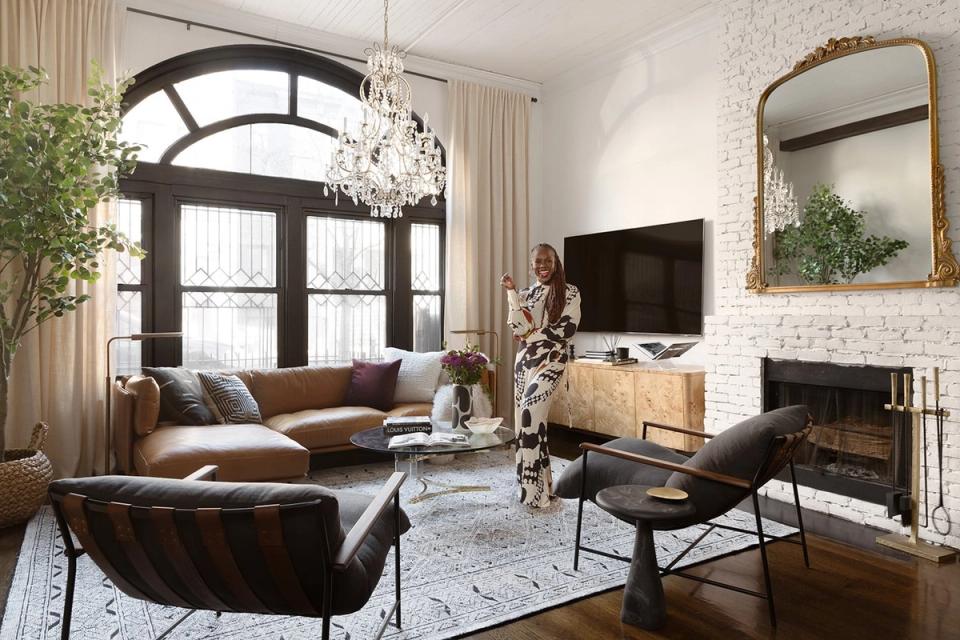Eclectic living room blending mid-century modern and contemporary styles with warm leather seating, crystal chandelier, and brick fireplace