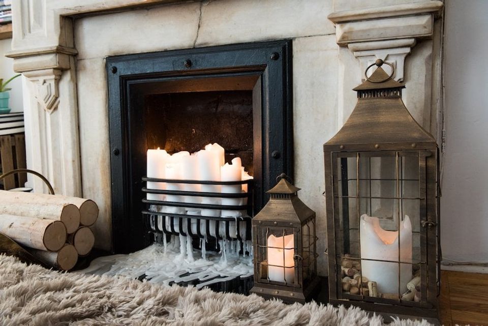 Hygge fireplace nook with warm lighting, vintage lanterns, cream fur rug, and rustic wood accents creating cozy Scandinavian ambiance
