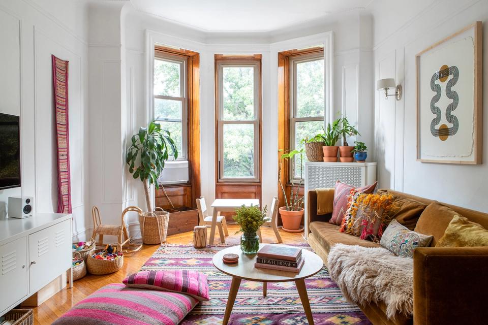 Eclectic bohemian living room with warm wood tones, colorful layered rugs, and abundant plants