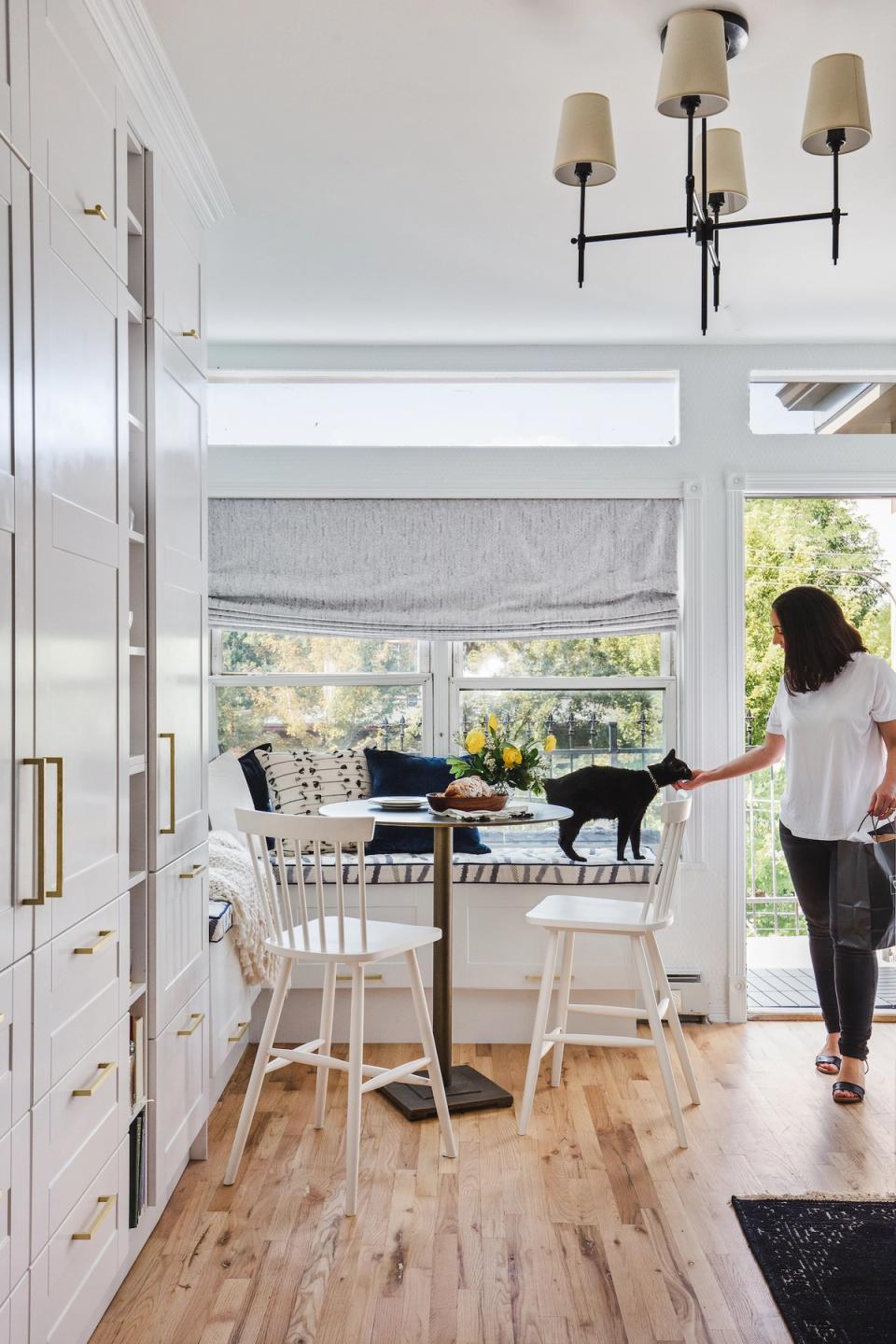 Bright, airy transitional dining nook with natural wood floors, white cabinetry, and modern black chandelier