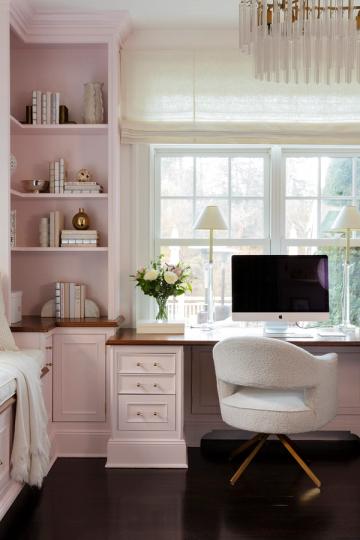 Soft pink home office with built-in shelving, window desk, and elegant brass-legged chair