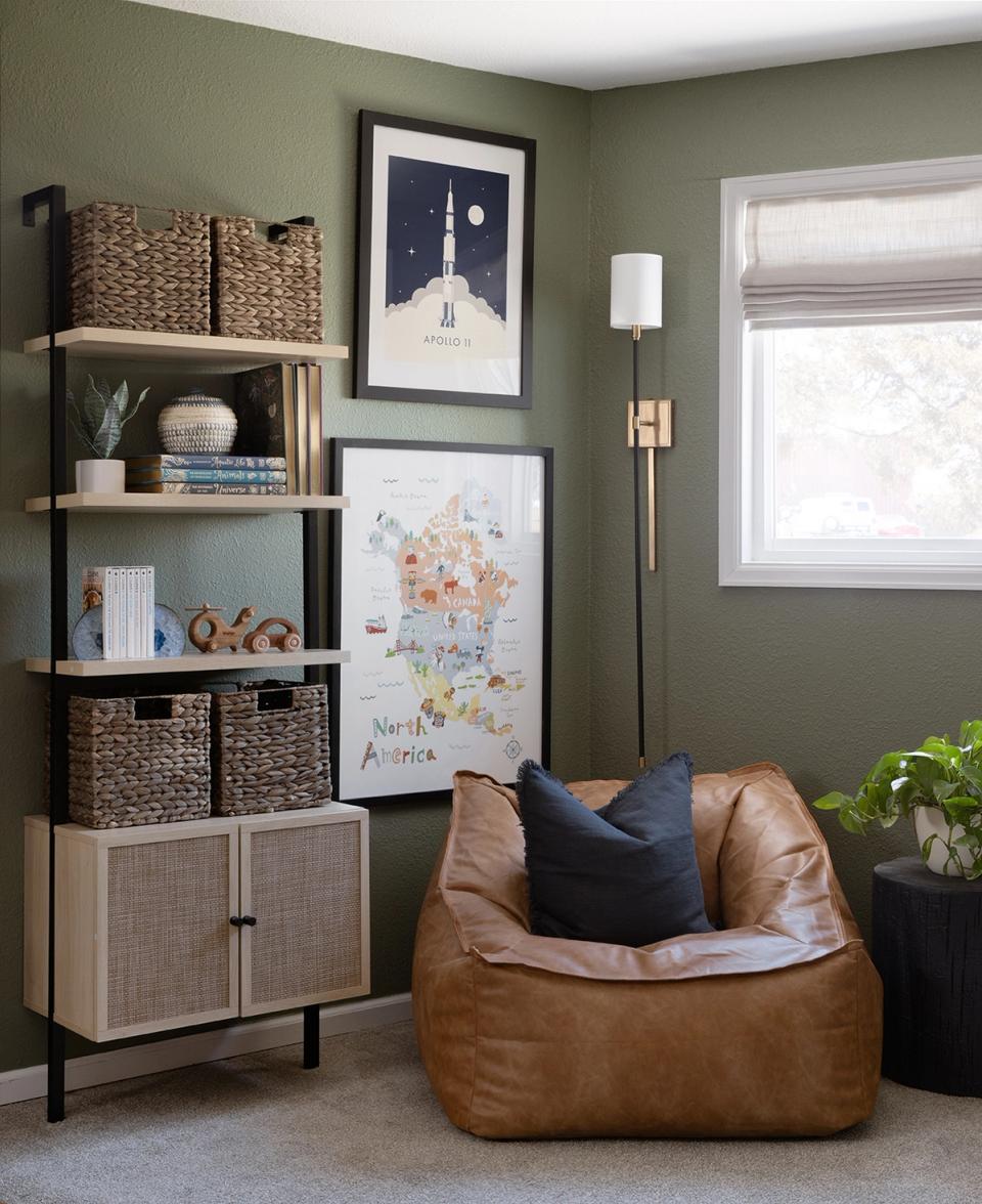 Sage green walls with cognac leather bean bag chair, natural wood shelving, and curated artwork in contemporary casual style