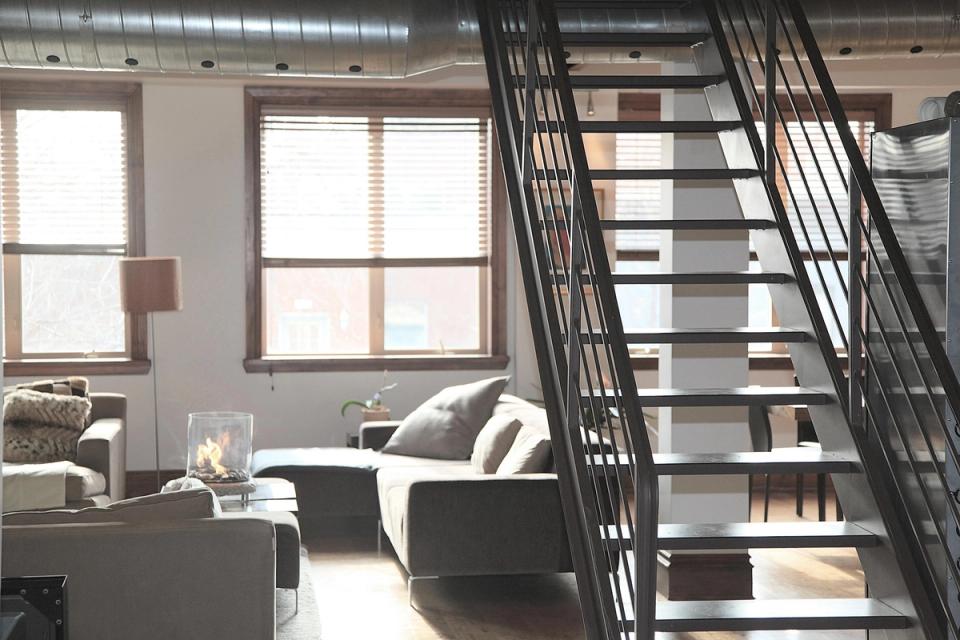 Industrial loft with black metal staircase, gray sofa, and bright windows creating an open, modern aesthetic