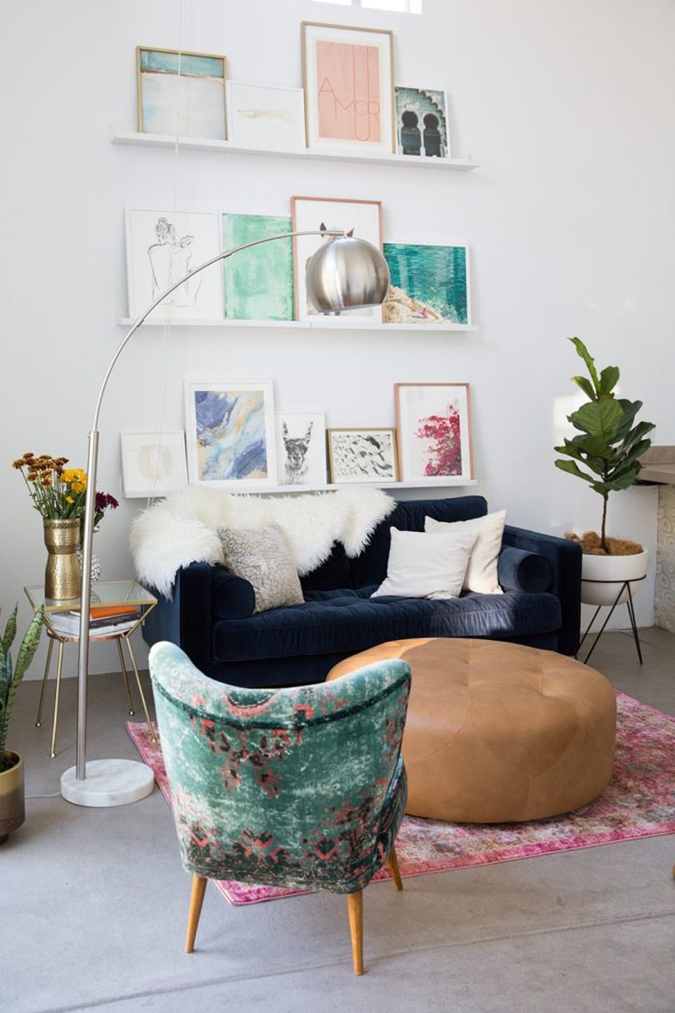 Modern eclectic lounge with floating gallery shelves, navy sofa, jewel-tone velvet chair, and colorful art prints.