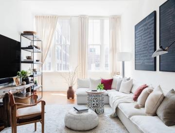 Scandinavian small living room featuring wall-mounted TV, soft neutral tones, natural light, vintage wood furniture, and cozy layered textiles