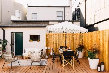 Modern minimalist deck with warm wood tones, mid-century wire chairs, striped awning, and clean Scandinavian aesthetic.