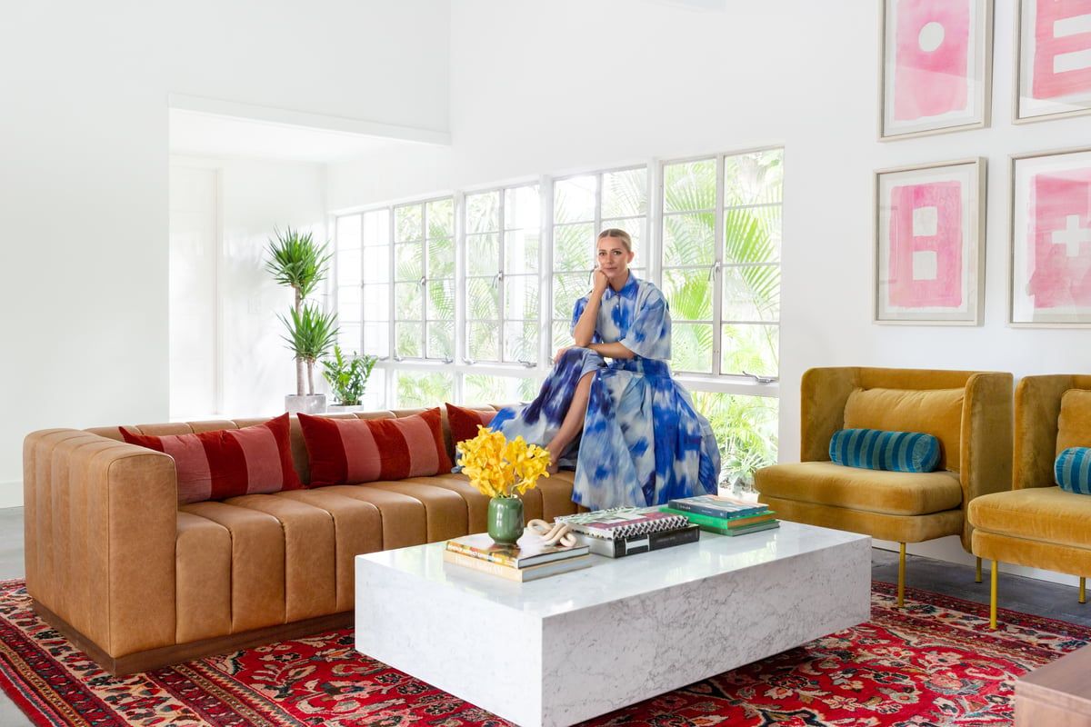 Bright, colorful living room with cognac leather sofa, mustard chairs, red patterned rug, and pink gallery wall art creating a cheerful, maximalist dopamine design aesthetic.