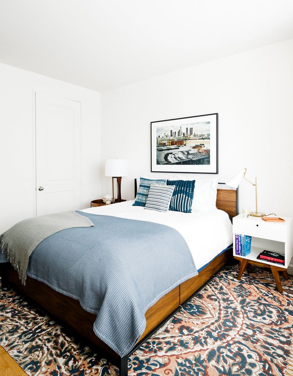 Warm mid-century bedroom blending wood tones, blue bedding, patterned rug, white floating shelves, and vintage-inspired styling