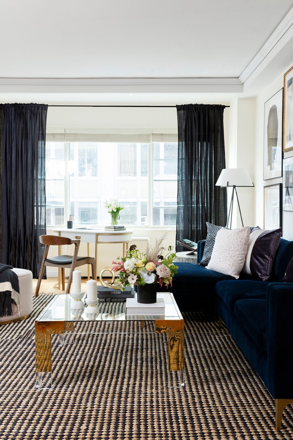 Modern living room with navy sofa, striped rug, black curtains, and natural light from large windows