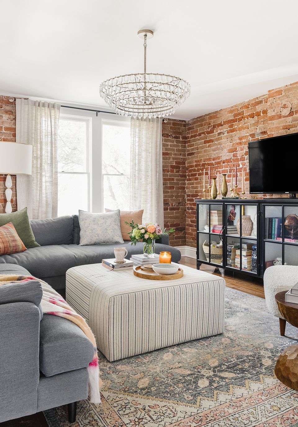 Industrial-glam living room featuring exposed brick accent wall, gray seating, and crystal chandelier