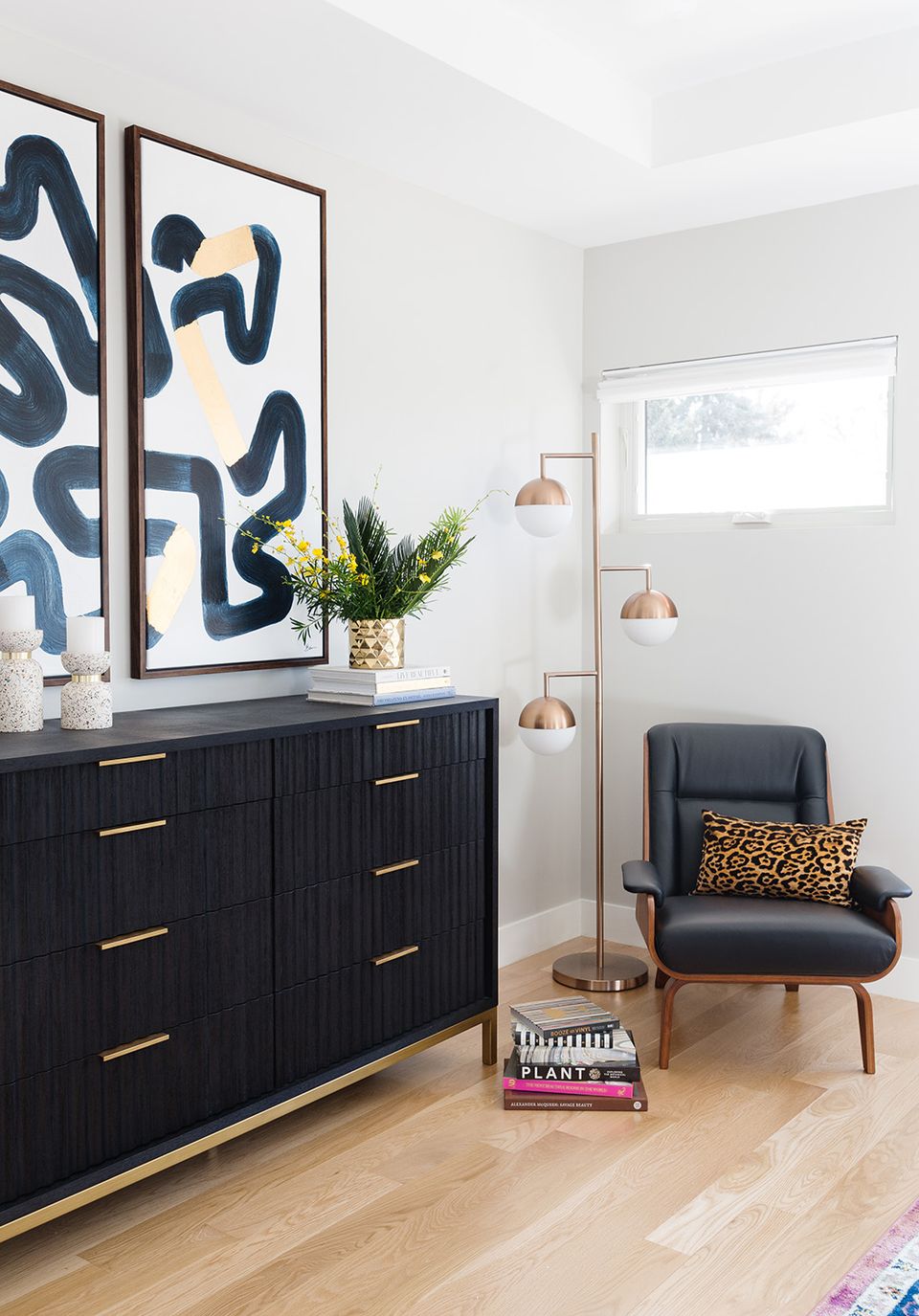 Modern sophistication with abstract navy wall art, black dresser with brass accents, and warm lighting creating a refined bedroom vignette.