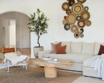 Eclectic boho living room featuring woven basket wall art, cream sectional with rust accents, and organic sculptural wood base table