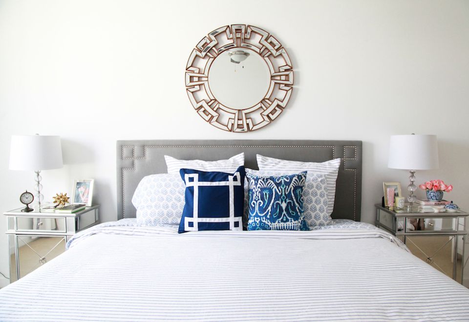Modern bedroom with gray upholstered headboard, white linens, and navy blue accent pillows