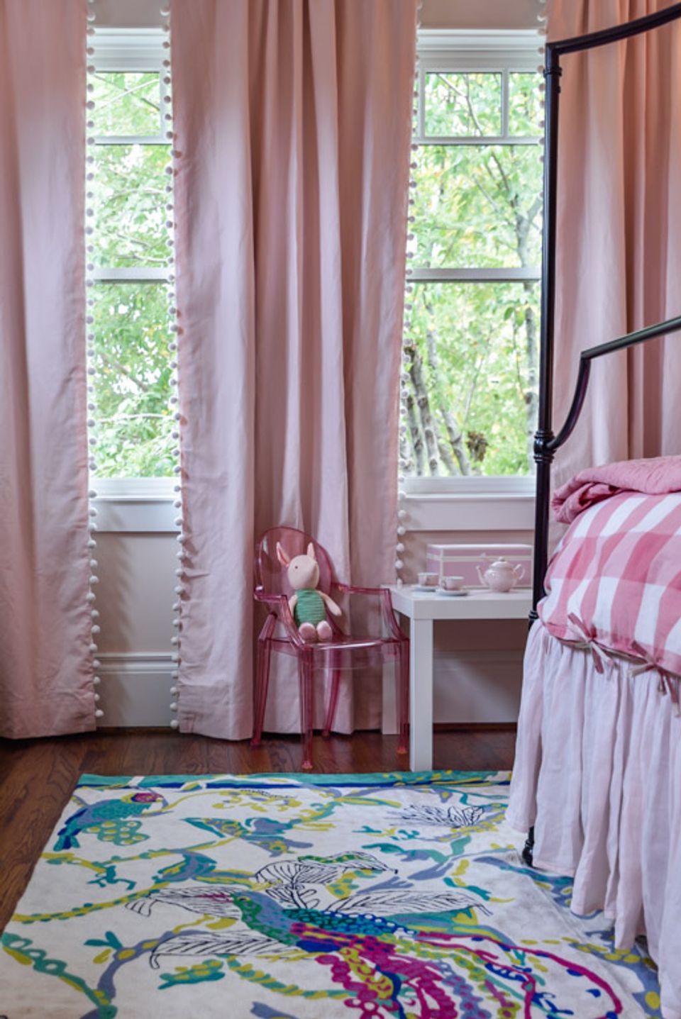 Floor-to-ceiling blush curtains with decorative trim frame windows overlooking greenery in a soft, romantic bedroom.