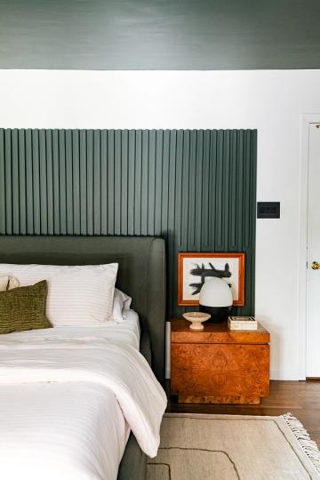 Contemporary bedroom with sage green paneled walls, white bedding, and wood nightstand